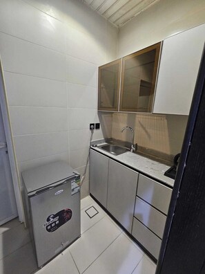 Una cuina compacta amb un rentapeus integrat, un refrigerador petit i un armari amb un mirall a la part superior.