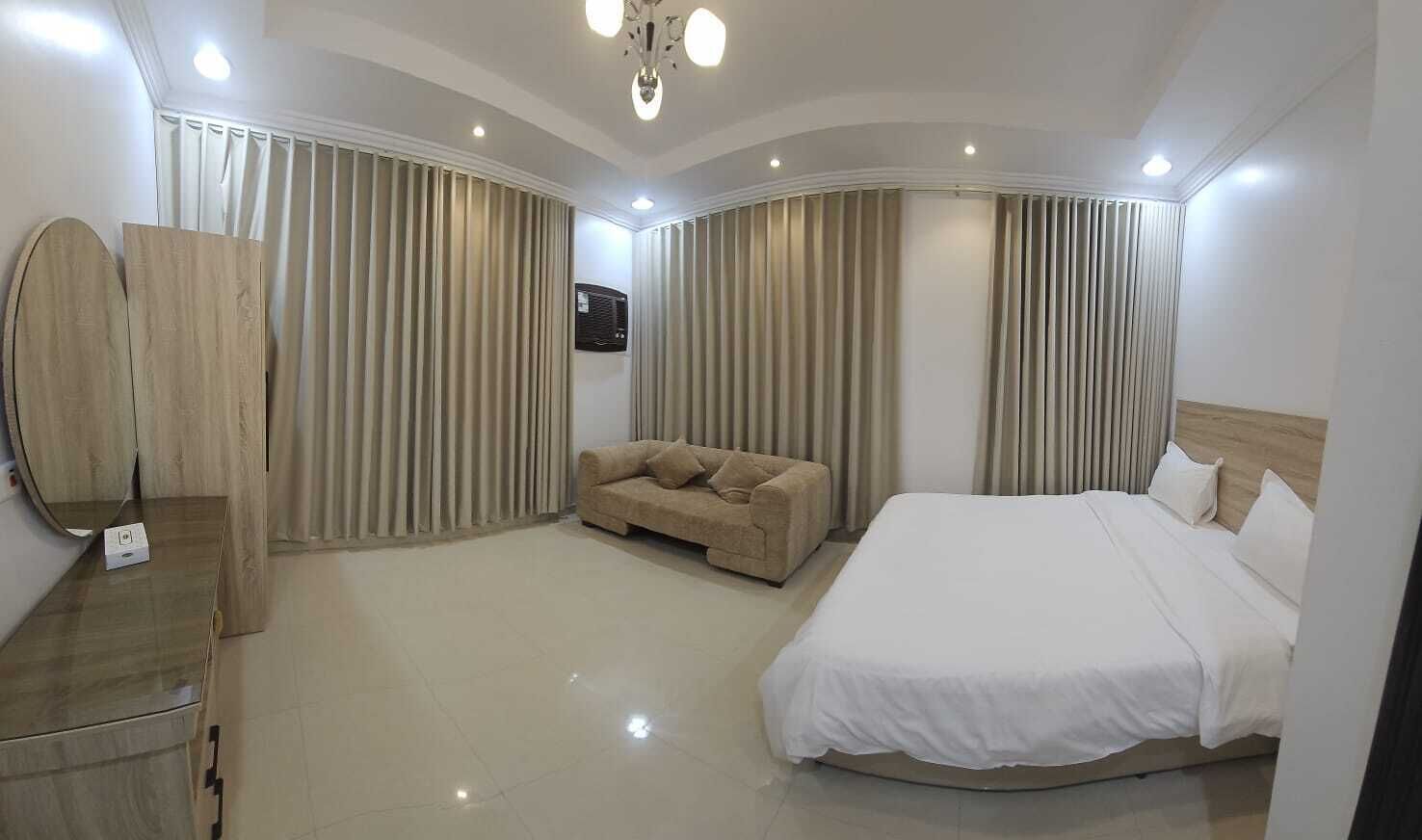 A hotel room with a large bed, a sofa, a mirror, and curtains.