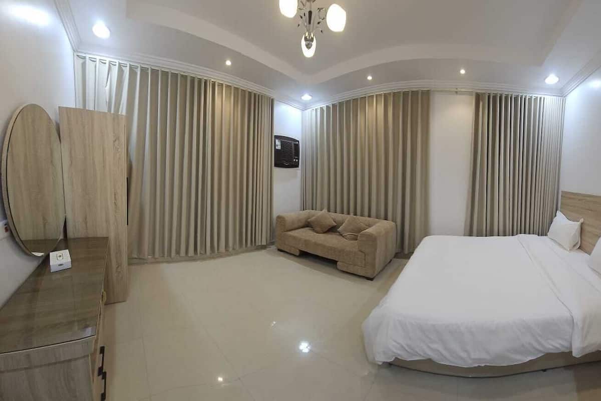 A hotel room with a large bed, a sofa, a mirror, and curtains.