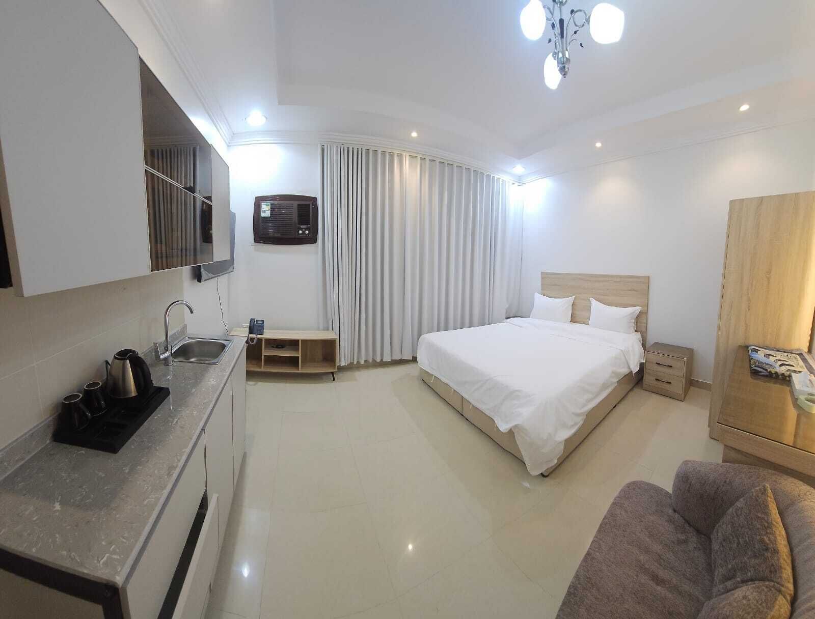 A hotel room with a bed, a sofa, a kitchenette, and a bathroom.