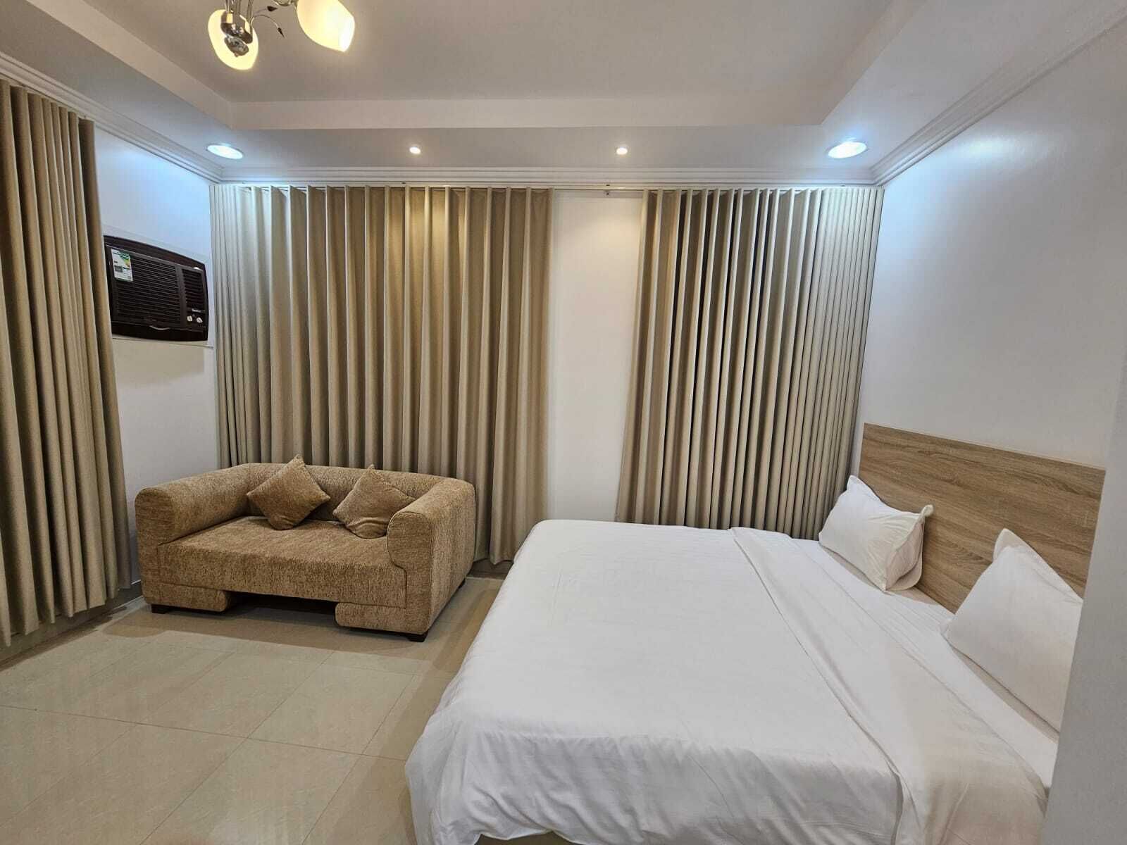 A hotel room with a bed, a sofa, curtains, and a ceiling light fixture.