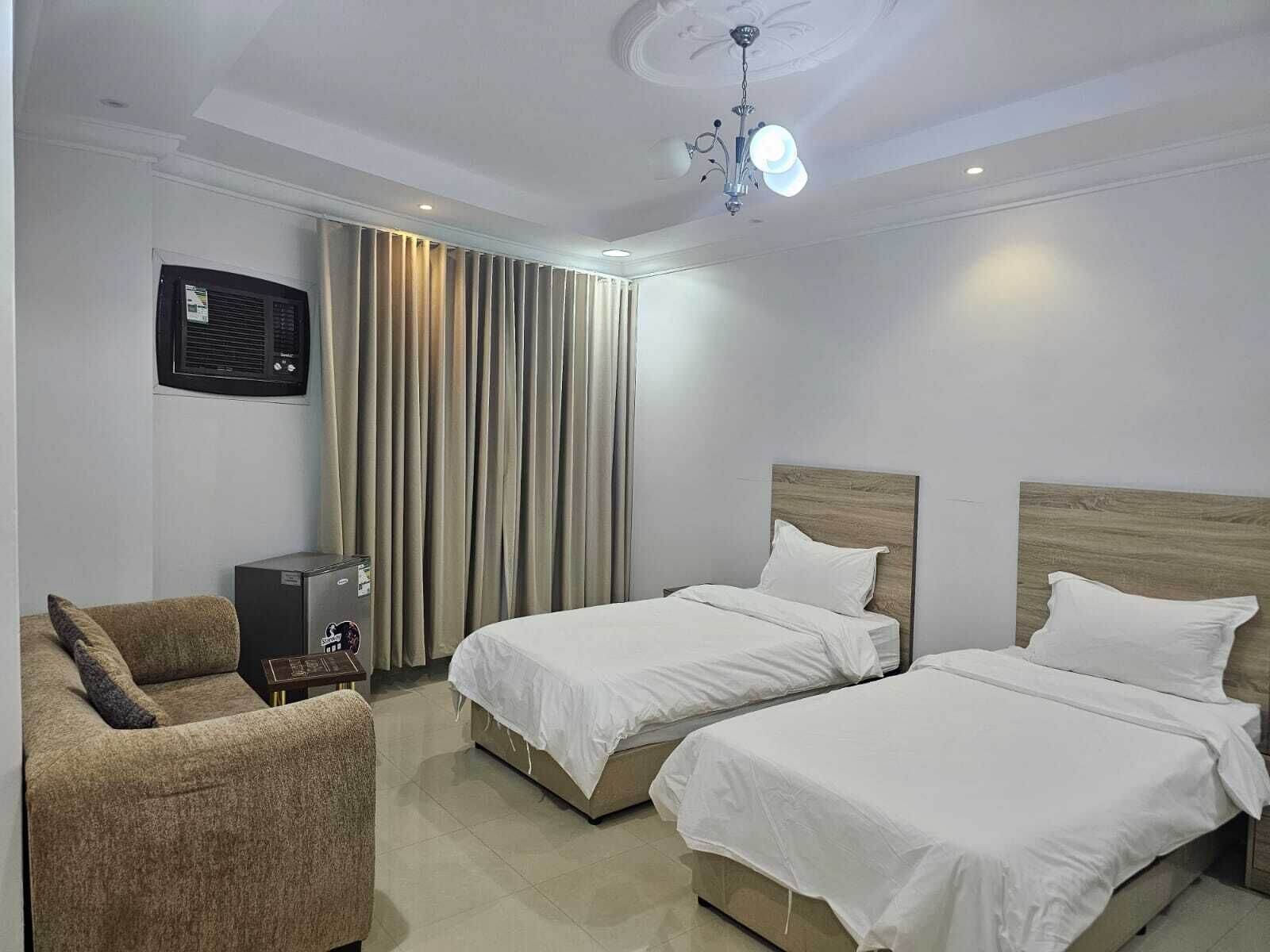 Habitación de hotel con dos camas, un sofá, un televisor y un ventilador de techo.