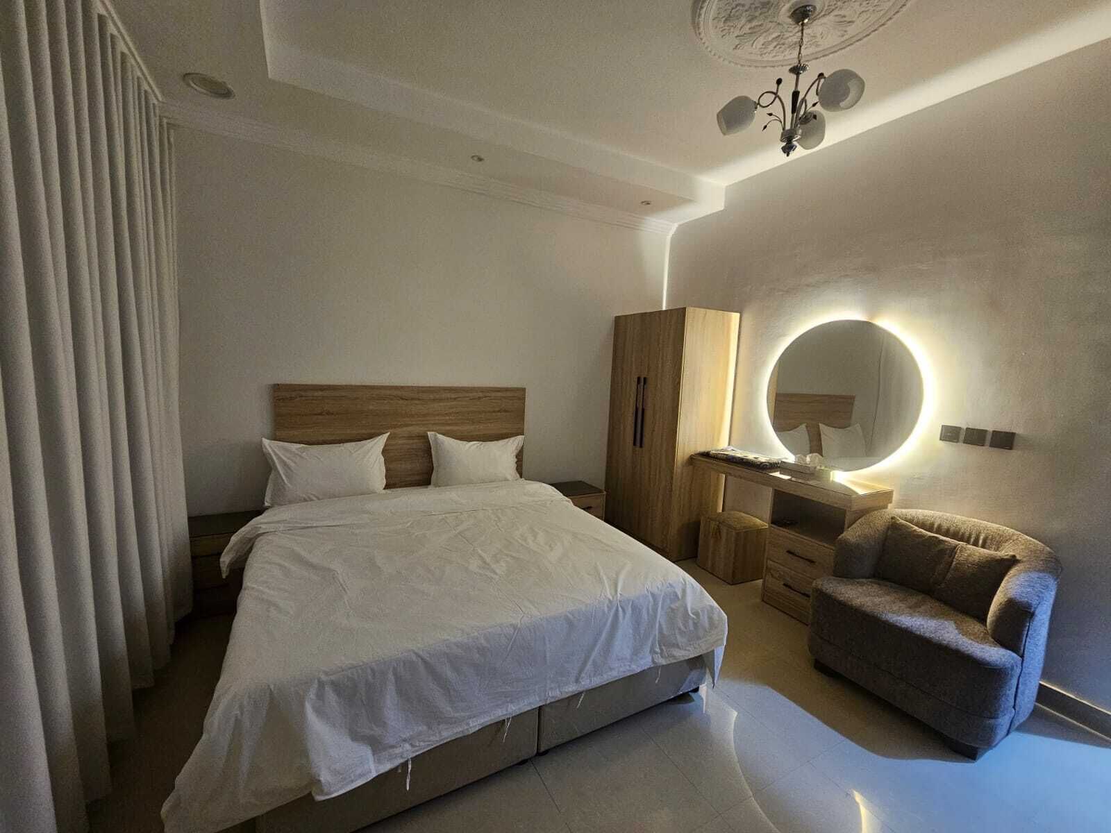 A modern bedroom with a large bed, a vanity with a mirror, a chair, and a ceiling light fixture.