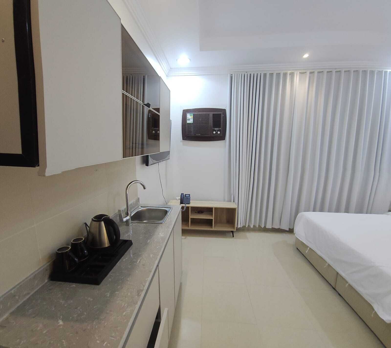 Habitación de hotel con kitchenette, una cama, un espejo, una ventana con cortinas y un equipo de aire acondicionado.