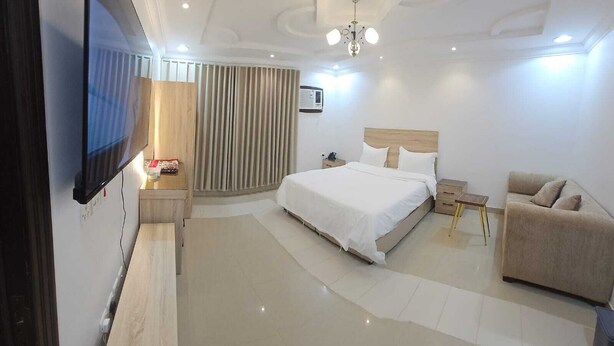 A modern hotel room with a large bed, a sofa, a TV, and a ceiling light.