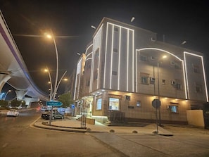 Um edifício com linhas verticais iluminadas, área de estacionamento e rua com veículos.