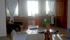 A cozy living room with a sofa, a coffee table, and a potted plant. There are wooden doors and a window with curtains. - Tranquil 1-bedroom apartment in charming Kingstown perfect for relaxing (Kingstown)