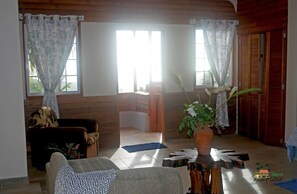 A cozy living room with a sofa, a coffee table, and a potted plant. There are wooden doors and a window with curtains. - Tranquil 1-bedroom apartment in charming Kingstown perfect for relaxing (Kingstown)