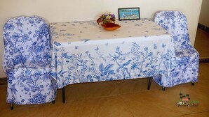 A table with a floral tablecloth, two chairs with matching covers, a small decorative bowl, and a framed picture on the table. - Tranquil 1-bedroom apartment in charming Kingstown perfect for relaxing (Kingstown)