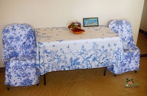 A table with a floral tablecloth, two chairs with matching covers, a small decorative bowl, and a framed picture on the table. - Tranquil 1-bedroom apartment in charming Kingstown perfect for relaxing (Kingstown)