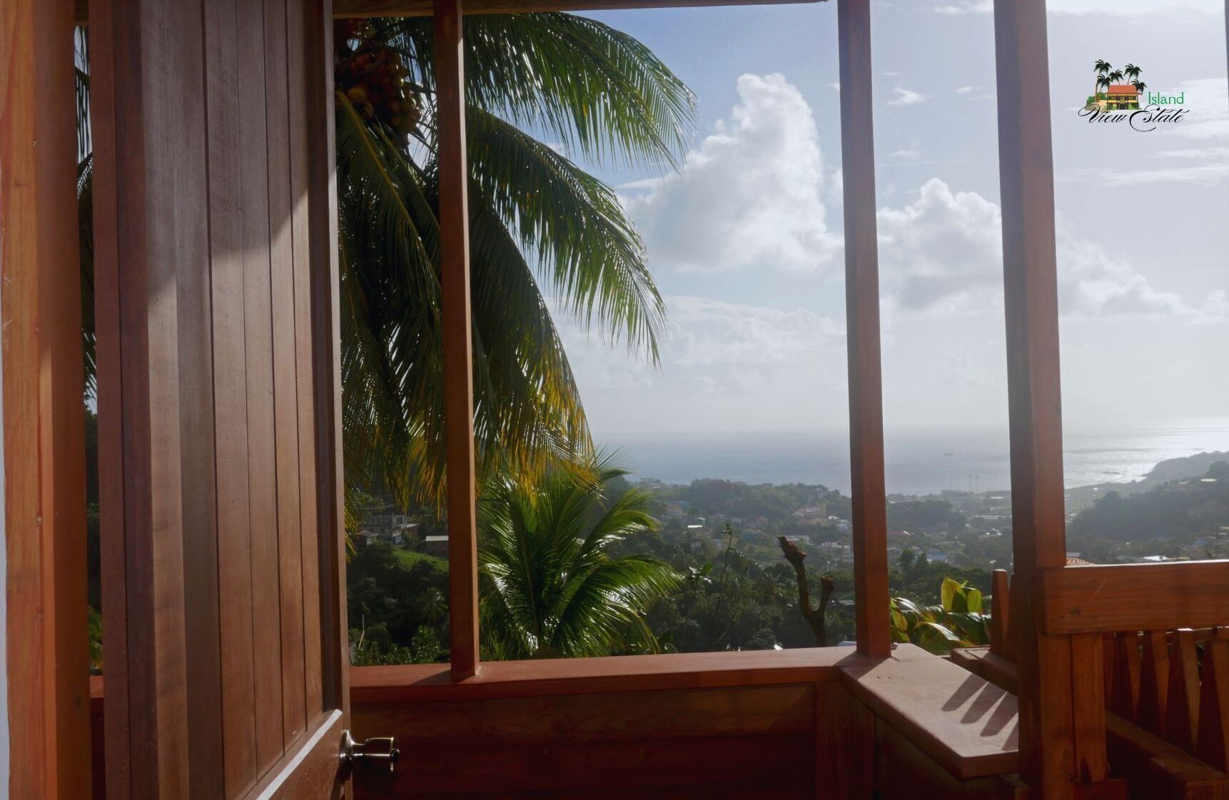 Ein Holzrahmenfenster mit Blick auf eine Küstenlandschaft, einschließlich Palmen und einer weiter entfernten Stadtansicht.