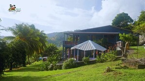 A two-story building with a covered outdoor area, surrounded by lush greenery and palm trees. - Tranquil 1-bedroom apartment in charming Kingstown perfect for relaxing (Kingstown)