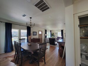 A spacious living area with a dining table, chairs, a chandelier, and a view through large windows.
