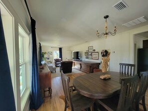 A dining area with a round wooden table, chairs, a chandelier, and a television on a wooden cabinet.