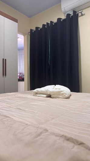 Una cama con un edredón blanco, una cortina negra y una pared blanca con un equipo de aire acondicionado.