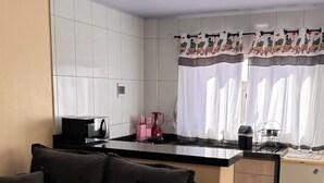 A modern kitchen with a black countertop, a built-in microwave, and a refrigerator. There is a black sofa with cushions in the living area.