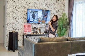 A person holding a microphone in a room with a television, a sign with motivational text, and a plant. - Sunday Villa Green Mellow Pattaya (Bang Lamung)