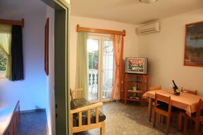 Ein Zimmer mit Esstisch, Stühlen, Fernseher und einer Schiebeglastür, die zu einem Außenbereich führt.