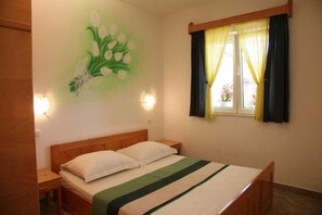 Ein Schlafzimmer mit Bett, Nachttisch, Wandlampe und einem Fenster mit Vorhängen.