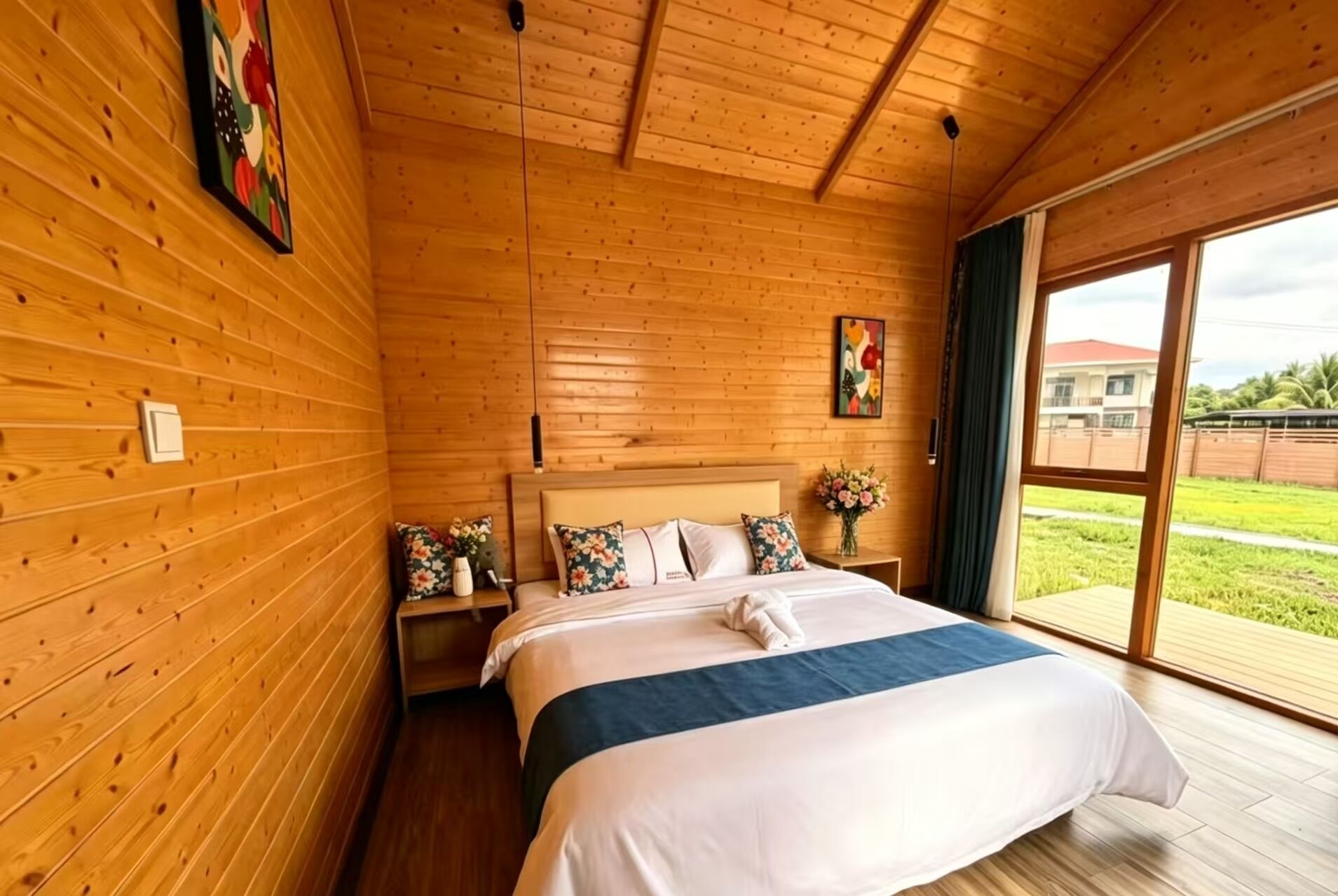 A wooden-paneled room with a bed, a nightstand, a vase of flowers, and a painting on the wall.