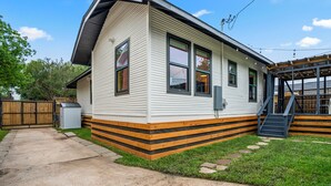 A single-story house with a covered porch, a small front yard, and a wooden fence. - EaDo Main House: Sleeps 12, Hot Tub Access, Near Downtown, NRG, Daikin & more (Houston)