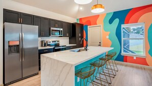 A modern kitchen with stainless steel appliances, a marble island, and bar stools. - EaDo Main House: Sleeps 12, Hot Tub Access, Near Downtown, NRG, Daikin & more (Houston)