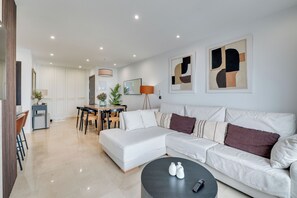 Ein modernes Wohnzimmer mit einem weißen Sofa, einem Esstisch mit Stühlen und einem Couchtisch mit zwei Vasen.