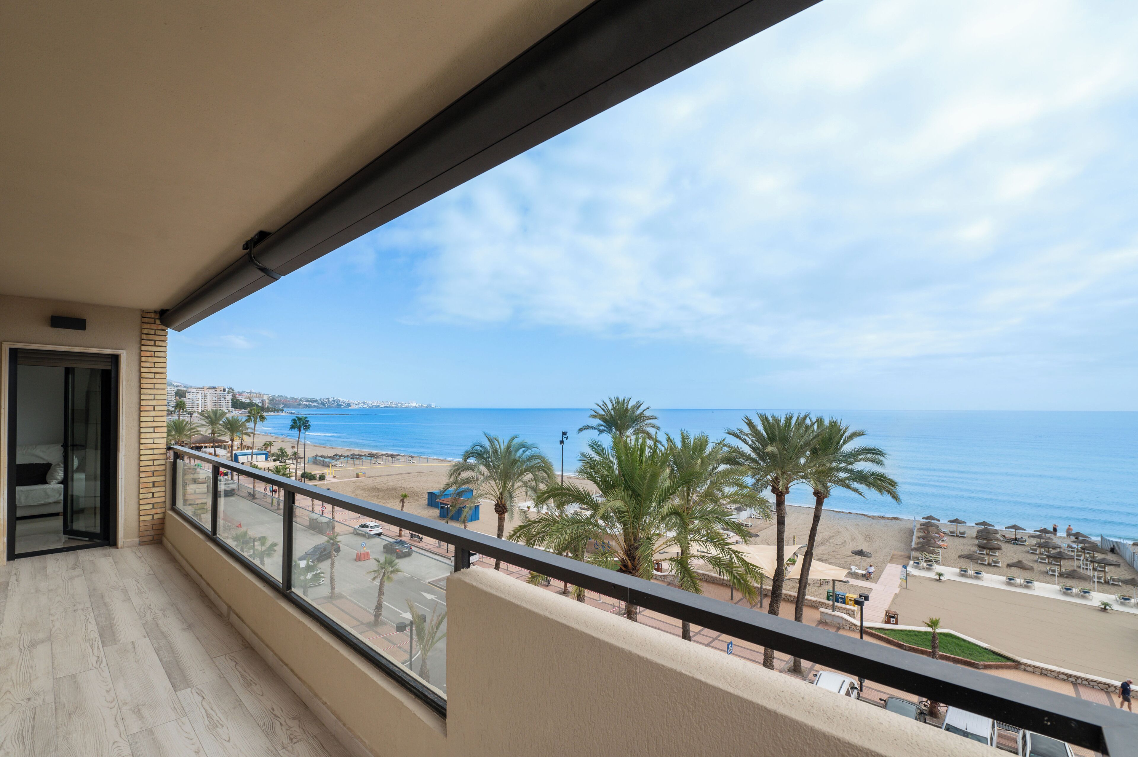 A balcony with a view of the beach, palm trees, and the sea.