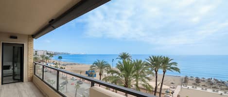 A balcony with a view of the beach, palm trees, and the sea.