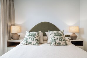 Ein ordentlich bezogenes Bett mit floralen Kissen, zwei Nachttischlampen und einem Kopfteil.