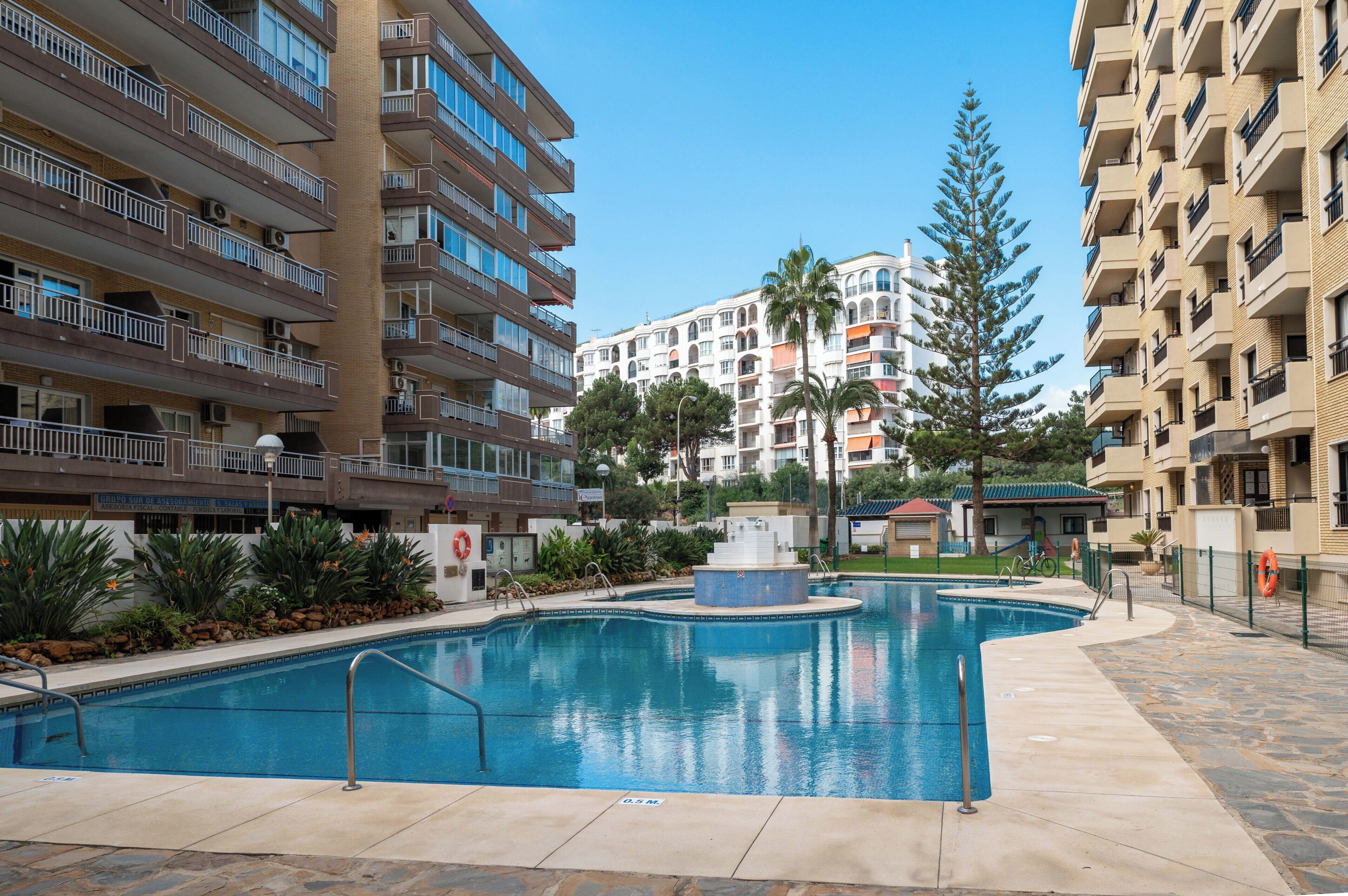 A swimming pool surrounded by apartment buildings, with a fountain in the center.