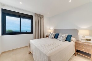 A bedroom with a large window, a bed with pillows, a nightstand with a lamp, and a view of the ocean. - LXR Matisse 2-Bedroom, Beachfront (Fuengirola)