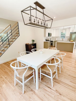 Una cocina moderna con armarios blancos, una mesa de comedor con sillas blancas y una escalera con barandilla de metal.