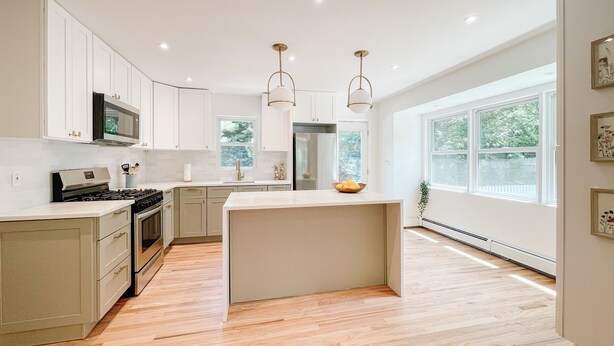 A modern kitchen with white cabinetry, a central island, stainless steel appliances, and pendant lighting.