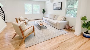 A spacious living room with a sofa, armchairs, a coffee table, and a large window with a view of trees.