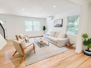 Un salón espacioso con sofá, sillones, una mesa de centro y un ventanal con vistas a árboles.