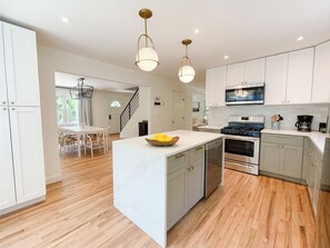 A modern kitchen with white cabinetry, a central island, stainless steel appliances, and a wooden floor.