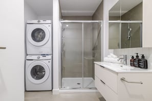 A compact bathroom with a washing machine, a shower enclosure, and a vanity with toiletries. - Maison Moderne | Balcony (Montreal)