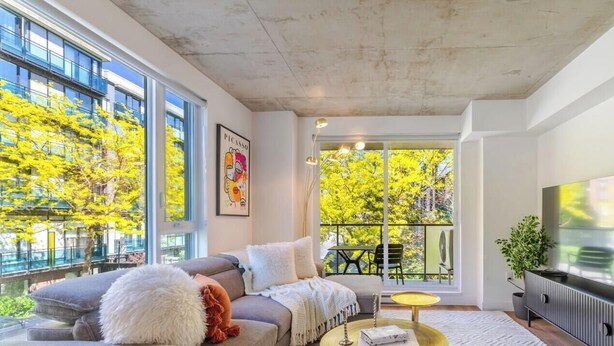 A modern living room with a sofa, a television, and a large window with a view of trees.