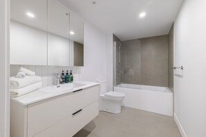 Une salle de bain moderne avec un grand miroir, un meuble-lavabo blanc, un lavabo, des toilettes et une douche à l’italienne.