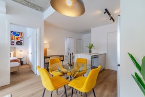 A modern apartment with a dining area featuring yellow chairs, a kitchen with a sink, and a living area with a sofa and a lamp. - City Escape | Balcony + BBQ (Montreal)