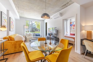 A modern living room with a glass dining table, yellow chairs, a sofa, and a TV. - City Escape | Balcony + BBQ (Montreal)