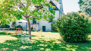 A building with a tree in the foreground, a grassy area, and outdoor furniture. - Peace, nature and old stones (Berthenay)