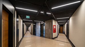 Un pasillo moderno de hotel con piso pulido, ascensor y señal de salida de emergencia.