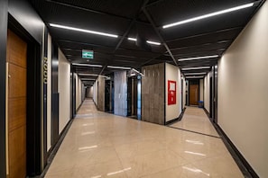 Corridoio moderno di un hotel con pavimento lucido, ascensore e cartello di uscita di emergenza.