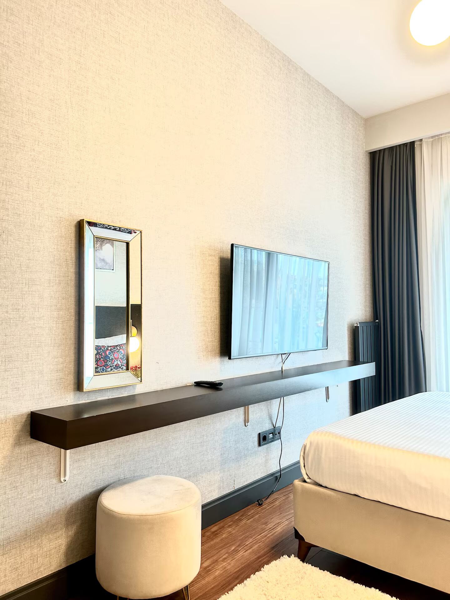 A hotel room with a bed, a TV mounted on a wall, a bedside table, and a mirror.