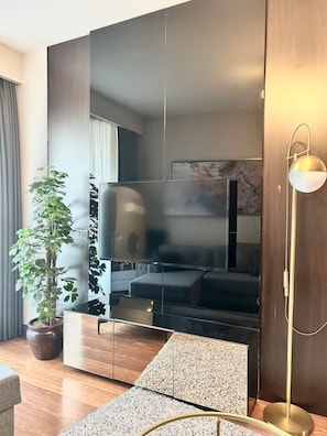 Un soggiorno moderno con una grande TV a schermo piatto, una pianta in vaso, una lampada da terra e un divano.