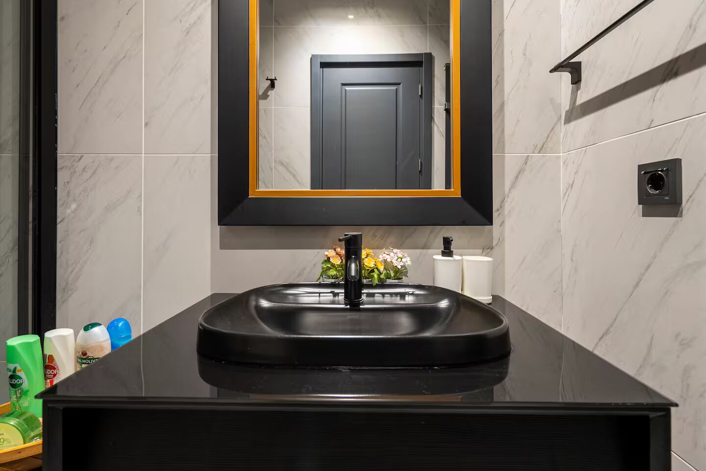 A modern bathroom with a black sink, a mirror with an orange frame, and toiletries on the counter.
