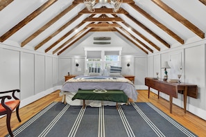 A bedroom with a sloped ceiling, wooden beams, a bed with a green runner, a bench, a nightstand, a dresser, and a window with blinds. - Charming Virginia Horse Country Retreat (Marshall)