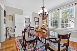 A dining room with a large wooden table, chairs, a chandelier, and a view of trees through large windows. - Charming Virginia Horse Country Retreat (Marshall)